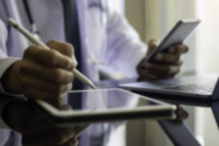 Blurred image of male doctor looking at phone and writing on tablet