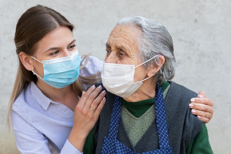 Caregiver with elderly person, both wearing masks