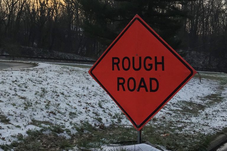 Rough road sign next to snow-covered median