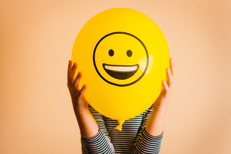 Child holding yellow balloon with smiley face on it