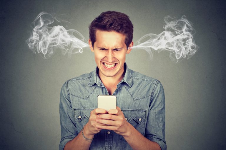 Frustrated angry man reading a text message on his smartphone blowing steam coming out of ears