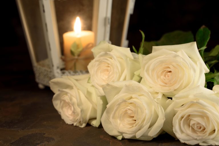 Beautiful white roses and candle on table against black background.