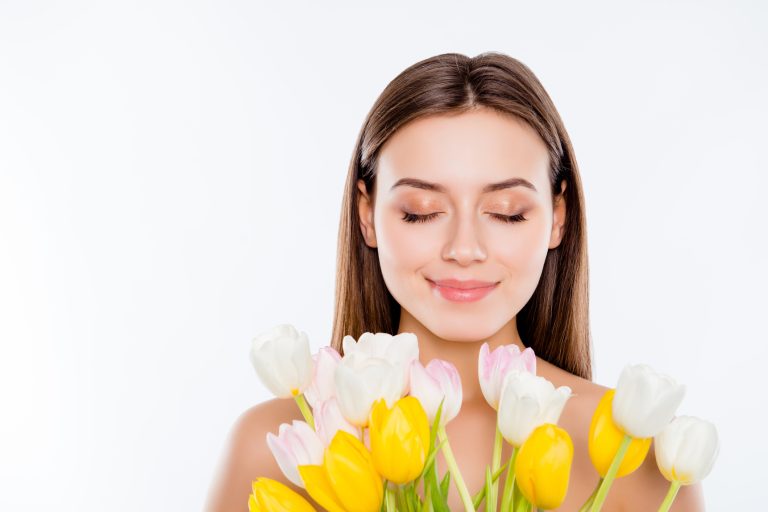 International women's day, wellbeing concept. Close up portrait of tender gentle woman with pure flawless face skin smelling aroma of tulips with close eyes isolated on white background