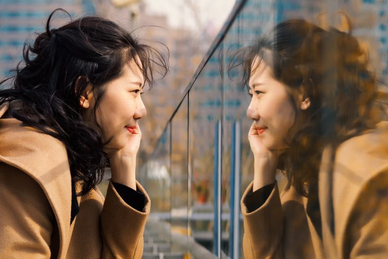 Beautiful Chinese girl looking at her mirror image in glass.