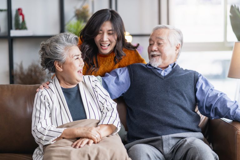 Elderly Asian parents sitting on couch with adult daughter behind them