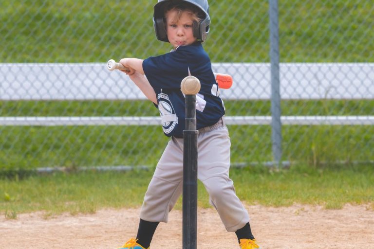 A photo of a Boy in a blue shirt mid-swing while trying to hit a ball off a tee.