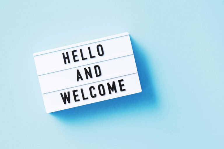 Light blue background, white sign with black lettering that reads "Hello and welcome"