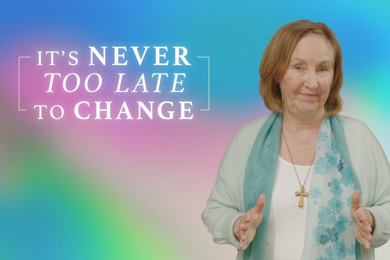 A woman encouragingly looks at the camera with the caption behind her "It's Never too late to Change." She is wearing a scarf and a cross around her neck and the background is a warm blue/pink/green blended color.