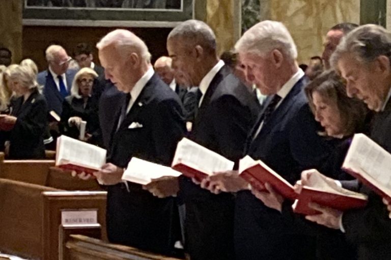 Presidents Biden, Obama, and Clinton, alongside Nancy Pelosi in a church pew. They are all reading out of red booklets as part of a funeral mass.