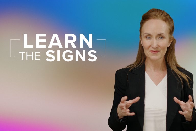 Woman with long brown hair, half pinned back. White shirt, black jacket with hands open and raised at the waist. Tagline reads "Learn the Signs"