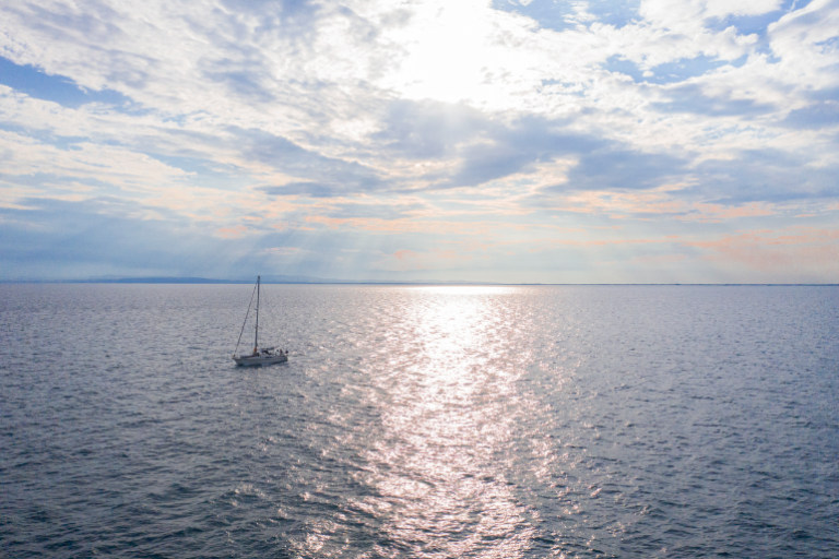 A small sailboat floats in the ocean as the sun shines over the open water